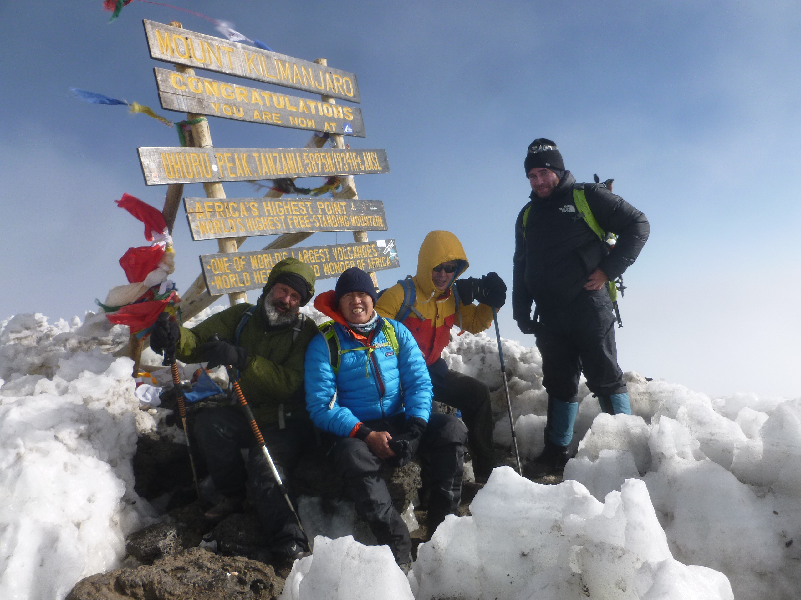 Team of successful hikers by the summit sign on Kilimanjaro