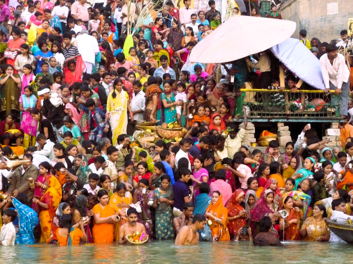 A wall of people in colorful dresses greet the sun at the edge of the Ganges