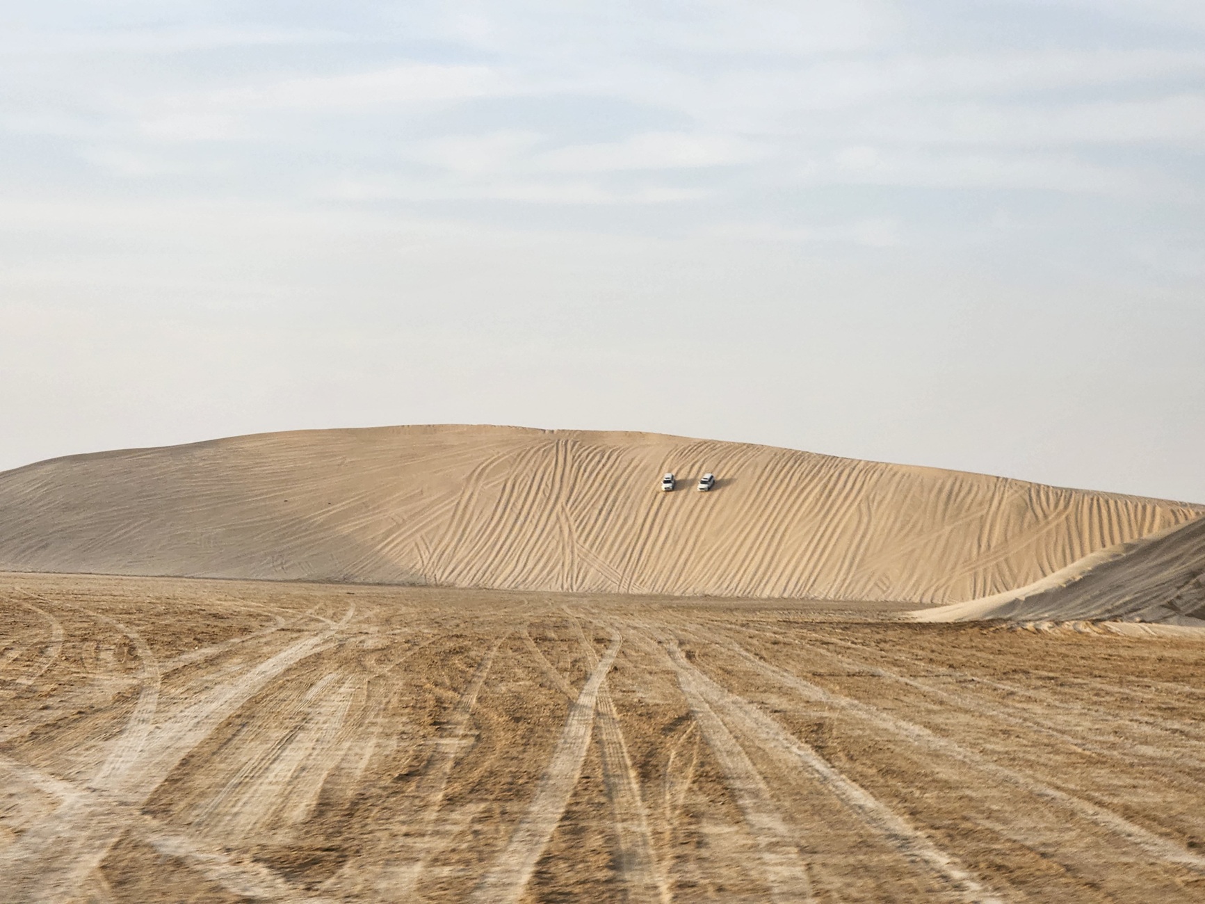 Two 4x4 SUVs drive down a dune while dune bashing in Qatar