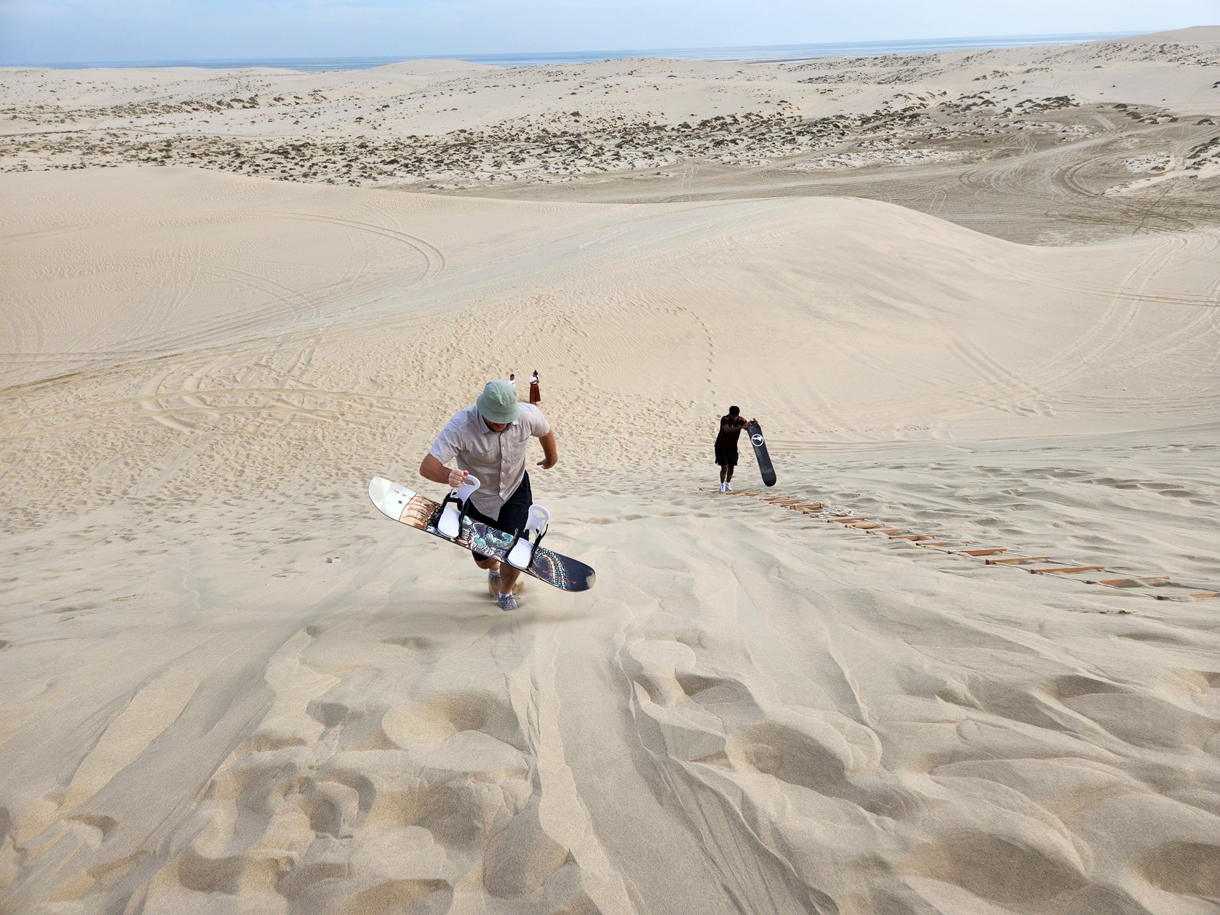 A person climbing up a sand dune while holding a board