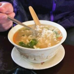 A bowl of hot thukpa, which contains noodles, vegetables, and soup.